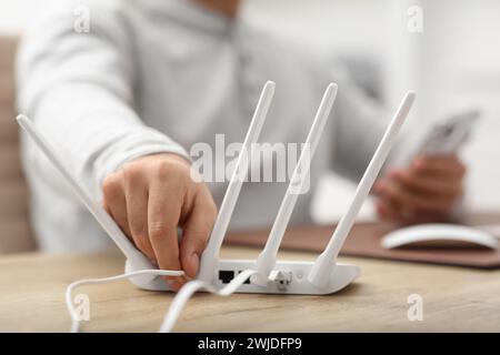 Mann, der Kabel in den WLAN-Router an einem Holztisch drinnen steckt, Nahaufnahme Stockfoto
