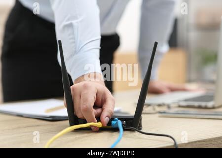 Mann, der Kabel in den WLAN-Router an einem Holztisch drinnen steckt, Nahaufnahme Stockfoto