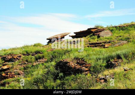 Alte Altäre in Form von flachen Steinen am sanften Hang eines hohen felsigen Hügels. Bergkampftruhen, Chakassia, Sibirien, Russland. Stockfoto