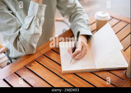 Eine Nahaufnahme eines Mannes, der in sein Notizbuch schreibt, Ideen aufschreibt oder ein Tagebuch führt, während er in einem Café sitzt. Stockfoto