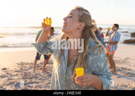 Junge kaukasische Frau mag es, Blasen am Strand bei Sonnenuntergang zu blasen Stockfoto