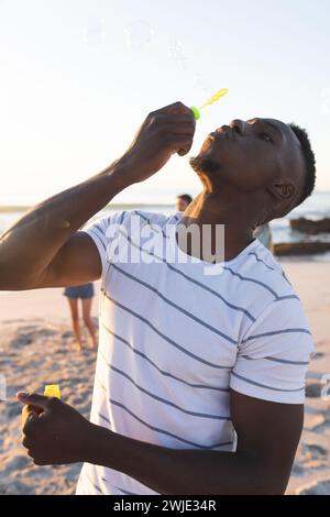 Junger afroamerikanischer Mann mag es, Blasen am Strand bei Sonnenuntergang zu blasen Stockfoto