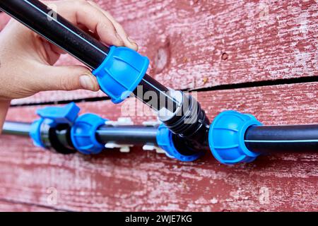 Ein externes Wasserversorgungssystem, das durch Kompressionsarmaturen verbunden ist, ist an der verwitterten Wand des roten Holzhauses montiert. Stockfoto