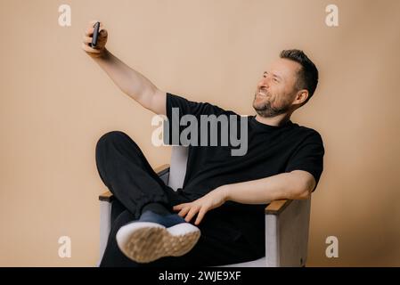 Mann lächelt und nimmt ein Selfie und Blog isoliert auf beigefarbenem Hintergrund Stockfoto