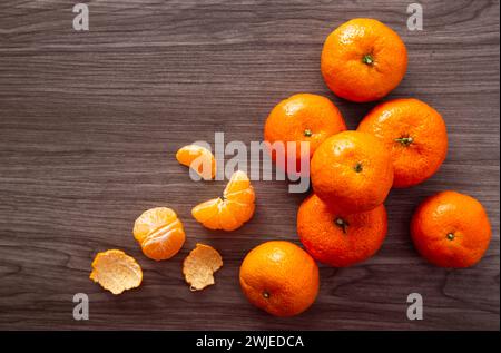 Tangerinen und geschälte Stücke liegen auf einer dunklen Holzoberfläche Stockfoto