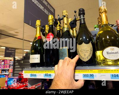 Lyon, Frankreich - 27. Dezember 2023: Eine männliche Hand greift nach einer Flasche teuren Dom Perignon Champagner zum Preis von 3023,90 in einem Supermarktgang Stockfoto