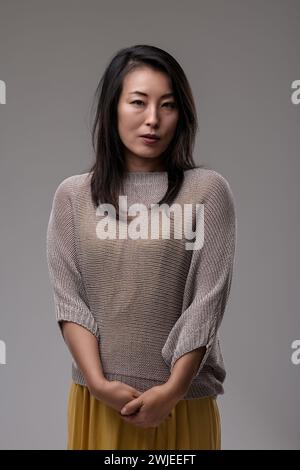 Die bewusste Frau in einem schicken Pullover und Rock strahlt Selbstvertrauen und eine raffinierte Luft aus, die Hände sanft umschlossen Stockfoto