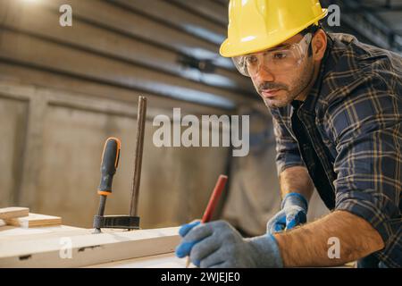 Zimmermann Tragen Sie bei der Arbeit Handschuhe und verwenden Sie ein Maßband und einen Bleistift, um ein Holzstück zu markieren Stockfoto