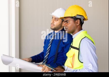 Das Team der Ingenieure, das mit der Arbeit des Architekten arbeitet, inspiziert das Bauprojekt der großen Gebäudefabrik mit Grundriss Stockfoto