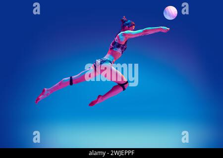 Wettbewerbsfähige Frau, begabter Volleyballspieler in Aktion, der sich auf Ball konzentriert, um perfekten Pass vor verlaufendem blauem Hintergrund in rosa Neonlicht zu dienen. Stockfoto