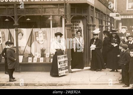 Kensington Women's Social & Political Union Ladenfront, Mary Sinclair steht vor dem Laden mit einem Poster „Victory Through Prison“, Kindern und anderen Suffragetten, Flugblättern, Fahnen und einem Bild von Emmeline Pankhurst im Schaufenster, Inschrift in Bleistift auf der Rückseite „Mary Sinclair, Kensington, 1910“ Stockfoto