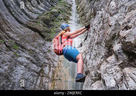 Klettererin auf Klettersteig neben dem Wasserfall, in Italien, Europa. Sommerabenteuer extreme Aktivitäten. Stockfoto