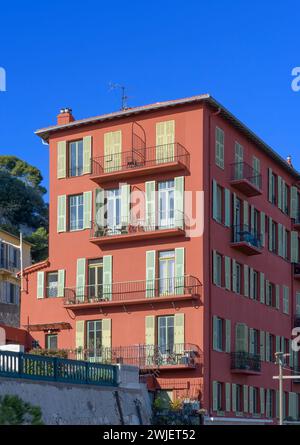 Schicke Apartments an der Küste von Nizza, an der französischen Riviera - Cote d'Azur, Frankreich. Herrliche Ockerfarben mit grau-grünen Fensterläden. Stockfoto