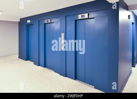 Zwei blaue Aufzüge und Tür zur Diensttreppe in der Lobby eines sanierten Sozialgebäudes Stockfoto