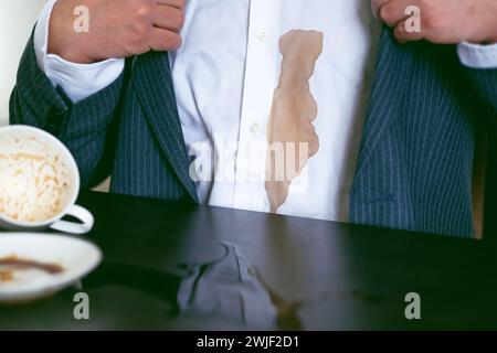 Ein Mann in einem Anzug verschüttete Kaffee auf ein weißes Hemd im Café. Dreckiger brauner Kaffeefleck auf der Kleidung. Daily Life Flin Concept. Stockfoto