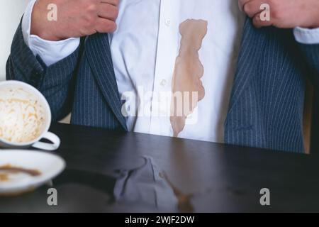 Ein nicht erkennbarer Mann verschüttete Kaffee oder Tee auf ein weißes Hemd. Daily Life Flin Concept. Stockfoto