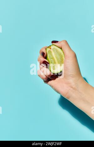 Unbekanntes weibliches Modell mit nagellack, das frische reife Limette in der Hand auf leuchtend blauem Hintergrund drückt Stockfoto