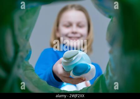 Ein Kind, das Plastikflaschen zu Hause im Papierkorb sortiert. Entsorgung Pflege Kosmetik oder Shampoo-Produkte. Stockfoto