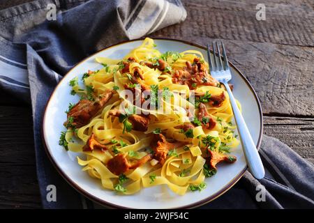 Tagliatelle Pasta mit gebratenen in Butter Pfifferlinge Pilze mit Knoblauch und fein gehackte Petersilie auf karierte Serviette auf einem rustikalen Hintergrund . Stockfoto