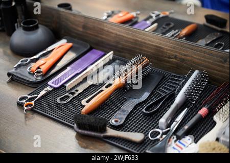 Nahaufnahme der Werkzeuge des Friseurs. Zugeschnittenes Foto von Friseurausrüstung auf Holztisch. Verschiedene Kämme und Bürsten liegen auf dem Hintergrund des Spiegels. Stockfoto