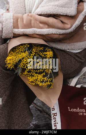 Modische Details aus beigefarbener warmer Jacke, braunem Rock und einem Blumenstrauß frischer Mimosa. Stylischer Winter-Look Stockfoto