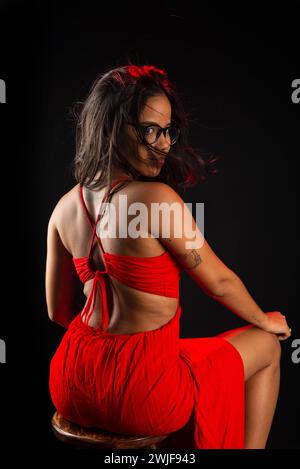 Salvador, bahia, Brasilien - 9. Dezember 2023: Schöne junge Frau mit Brille in rotem Outfit sitzend posierend zum Foto. Isoliert auf Blac Stockfoto