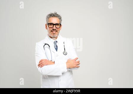 Mit einem freundlichen Lächeln und einem professionellen Auftreten strahlt dieser leitende Arzt Zugänglichkeit und Erfahrung aus und steht bereit in einem weißen Labormantel mit Stethoskop vor einem sauberen, weißen Hintergrund. Stockfoto