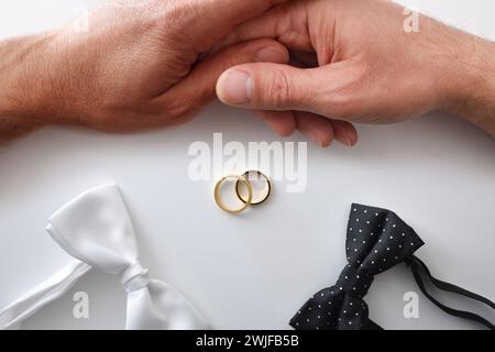 Konzeptueller homosexueller Hochzeitshintergrund mit schwarz-weißer Fliege, Eheringe in der Mitte und Paare, die Hände halten. Draufsicht. Stockfoto