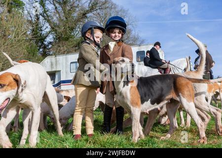 Arley, Worcestershire, Großbritannien. Februar 2024. Die vierjährige Myla Mills und ihre Freundin Rosa, die während der Halbzeit nicht in der Schule sind, begrüßen die Hunde in einem Rasentreffen der Albrighton and Woodland Hunt in Arley, Worcestershire, an einem ungewöhnlich warmen Tag. Ein Rasentreffen geht normalerweise einer Jagd voraus und findet auf privatem Gelände statt. Quelle: Peter Lopeman/Alamy Live News Stockfoto