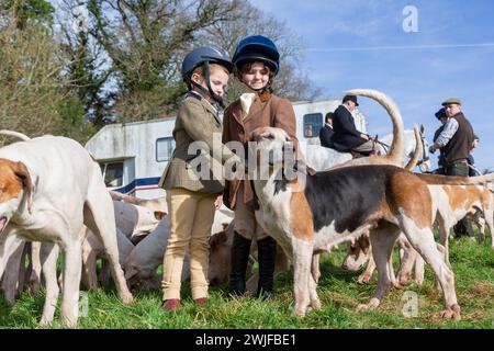 Arley, Worcestershire, Großbritannien. Februar 2024. Die vierjährige Myla Mills und ihre Freundin Rosa, die während der Halbzeit nicht in der Schule sind, begrüßen die Hunde in einem Rasentreffen der Albrighton and Woodland Hunt in Arley, Worcestershire, an einem ungewöhnlich warmen Tag. Ein Rasentreffen geht normalerweise einer Jagd voraus und findet auf privatem Gelände statt. Quelle: Peter Lopeman/Alamy Live News Stockfoto