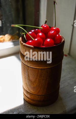 Auf der Fensterbank steht ein Holzbecher mit einer roten Kirsche. Stockfoto