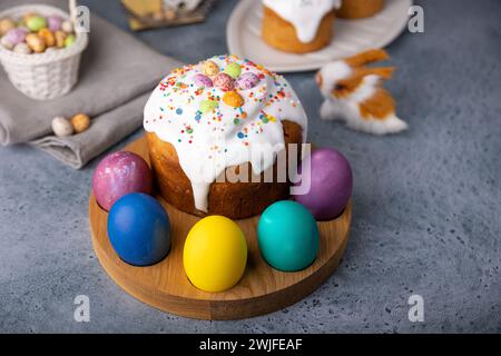 Osterkulich mit kandierten Früchten in weißer Glasur mit bunten Streuseln und bemalten Eiern. Traditionelles Ostergebäck. Osterferien. Nahaufnahme, wählen Sie Stockfoto