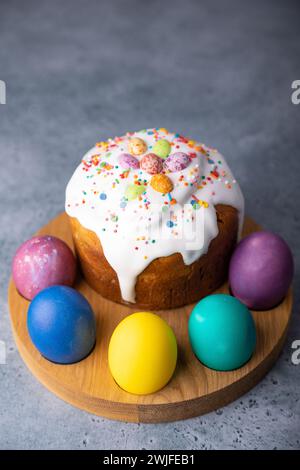 Osterkulich mit kandierten Früchten in weißer Glasur mit bunten Streuseln und bemalten Eiern. Traditionelles Ostergebäck. Osterferien. Nahaufnahme, wählen Sie Stockfoto
