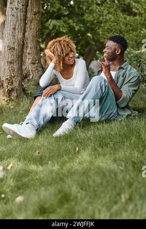 Gebärdensprache, positives afroamerikanisches Paar, das mit Gesten kommuniziert und auf Gras sitzt Stockfoto