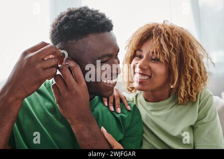 Tauber und glücklicher afroamerikanischer Mann mit Hörgerät in der Nähe von Freundin, Gesundheitsgerät Stockfoto