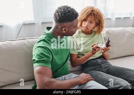 Taube afroamerikanerin, die Hörgerät in einer Kiste neben dem Freund hält, während sie auf der Couch sitzt Stockfoto