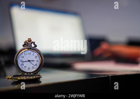 Die Zeit ist einfach vergangen. Eine klassische Taschenuhr, die vor einem geschäftigen Schreibtisch mit Laptop steht Stockfoto