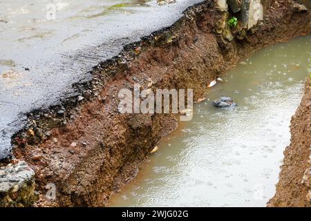 Erosion von Straßenasphalt um Entwässerungskanäle in Wohngebieten Stockfoto