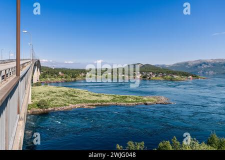 Die Saltstraumen Bridge erhebt sich über den stärksten Strudel der Welt, mit wirbelnden Strömungen darunter und einem malerischen Dorf in der Ferne Stockfoto