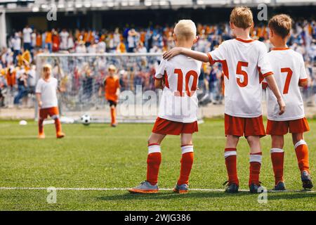 Schuljungen als Fußballfreunde. Kinder haben sich während des Elfmeterschießspiels in einem Sportteam vereint. Kinder in Fußballuniformen in einer Sportarena Stockfoto