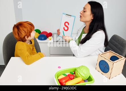 Sprach- und Sprachtherapie bei Kindern. Gutaussehender Junge, der den Buchstaben S mit dem Sprachpathologen in der Praxis des Logopäden ausspricht Stockfoto