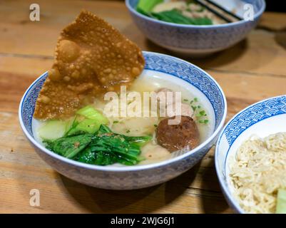 Mie Pangsit, eine Schüssel Fleischbällchensuppe mit frischem Gemüse auf dem alten Holztisch. Stockfoto