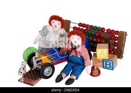Raggedy Ann & Andy, alte handgemachte Stoffpuppen, sitzen umgeben von Vintage-Spielzeug; Holzklötze, Ball, Rennwagen, Hund, Schachfiguren, Hut, Perlenzähler. Stockfoto