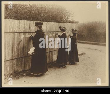 Historisches Suffragettes Bild von Frauen, die auf einem Holzzaun „Vots for Women“ schreiben, mit dem Ort des nächsten Treffens. Aus den Zeitungen von Bessie Rischbiet, der australischen Führerin der Bewegung. Stockfoto