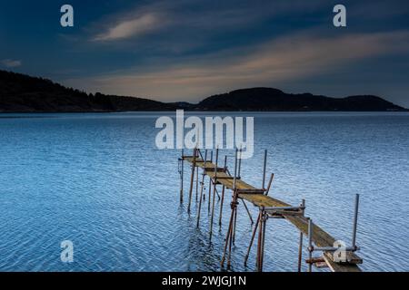 Meereslandschaft mit Holzbrücke, die sich ins Meer erstreckt. Weißes hartes Licht im Stil Stockfoto