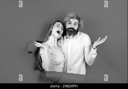 Überraschte ein Paar bärtiger Männer und glücklicher Frauen, die ein Loch im Papier machten und durch ein Loch suchten. Werbetafel, blauer Hintergrund. Durch Loch in koppeln Stockfoto