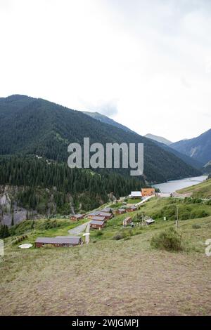 Traditionelles Kasachstans Jurtencamp im malerischen Bergtal in der Nähe des Flusses. Gemütliche Filz- und Holzjurten bieten lokale Gastfreundschaft inmitten von schneebedeckten Gipfeln. Stockfoto