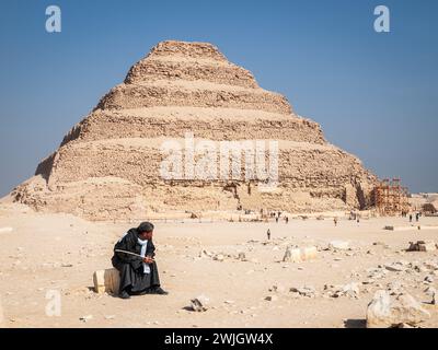 Ägyptischer Mann, der an einem sonnigen Tag vor der Stufenpyramide von Zoser sitzt, Sakkara Nekropolis, Gizeh, Ägypten. Stockfoto