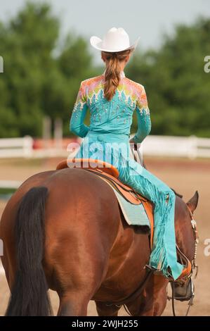 Junge Mädchen oder Cowgirl weiblich in Reitwettbewerb westliche Kleidung Pferdeschau Kleidung Cowboyhut und Chaps und Westernhemd sitzen auf Pferd Stockfoto