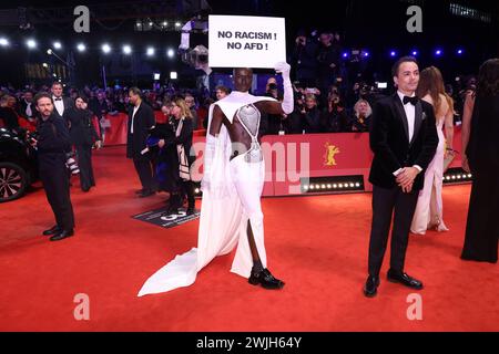 Berlin, Deutschland. Februar 2024. Papis Loveday (M) steht am Eröffnungsabend der Berlinale mit einem Protestzeichen "kein Rassismus! Kein AFD!' Auf dem roten Teppich. Auf der rechten Seite ist der Schauspieler Nikolai Kinski. Die 74. Internationalen Filmfestspiele Berlin finden vom 15. Bis 25. Februar 2024 statt. Quelle: Gerald Matzka/dpa/Alamy Live News Stockfoto